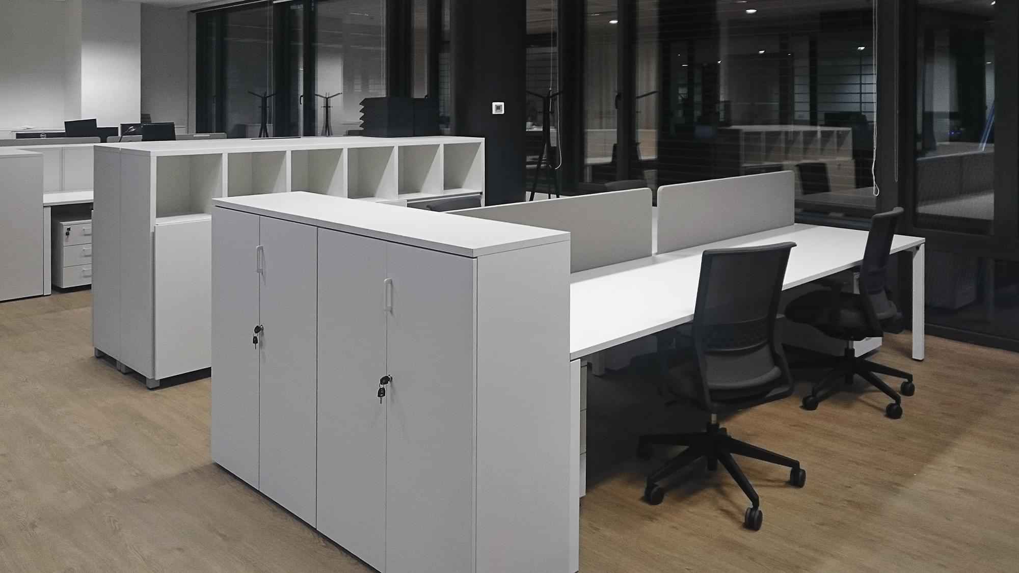 Pracovní místa jsou vybavená bílými stoly, bílými skříněmi a černými židlemi. 