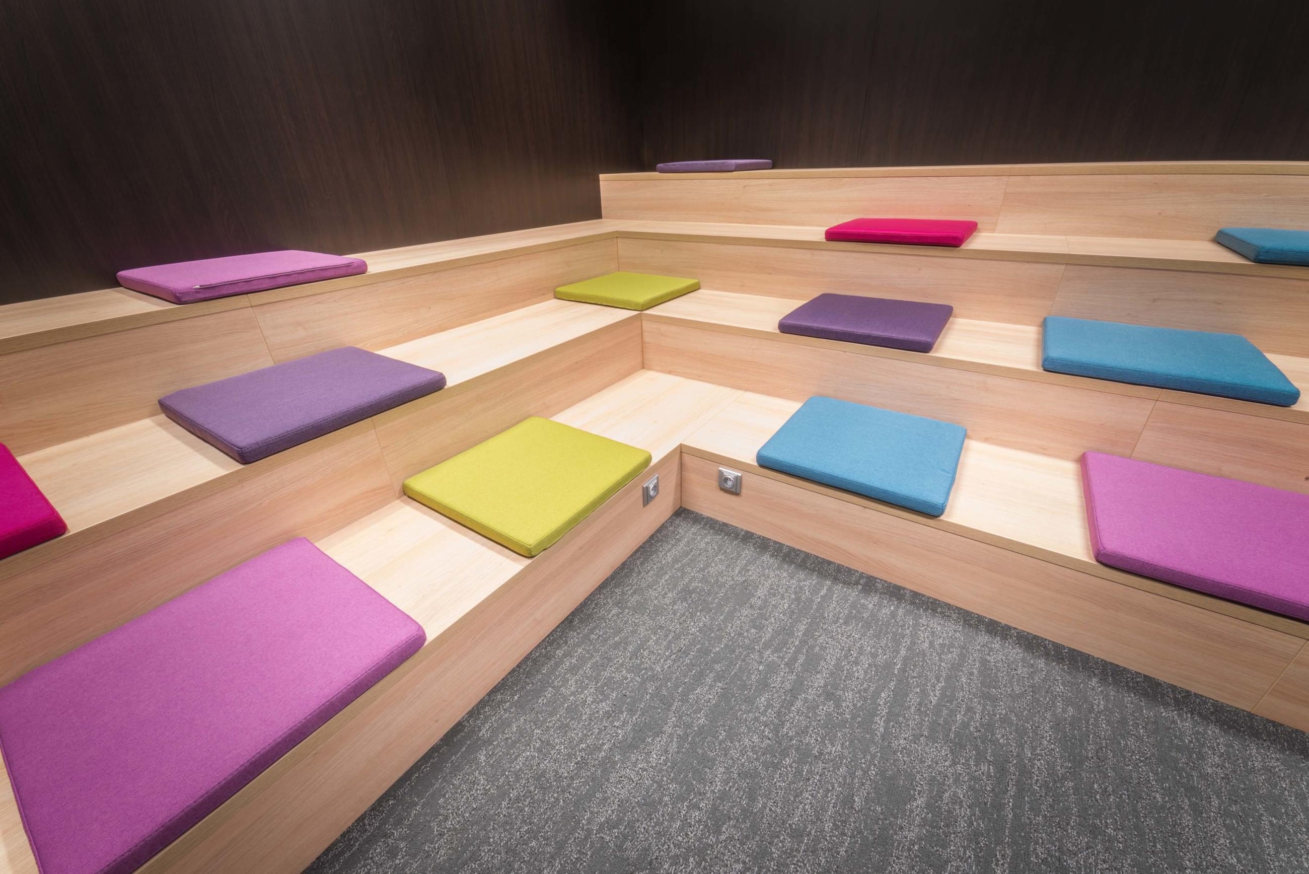 zasedací-místnost-Wargaming-Prague-kaskádovitá-dřevěná-lavice-barevné-podsedáky-CAPEXUS