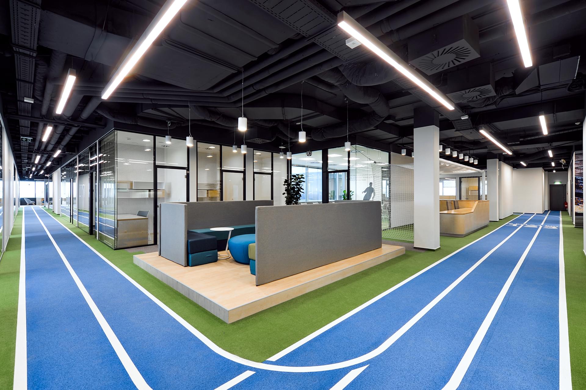 Světlé otevřené zasedací místnosti ve firmě SPORTISIMO rozděluje modrá běžecká dráha, která proplouvá celým interiérem.