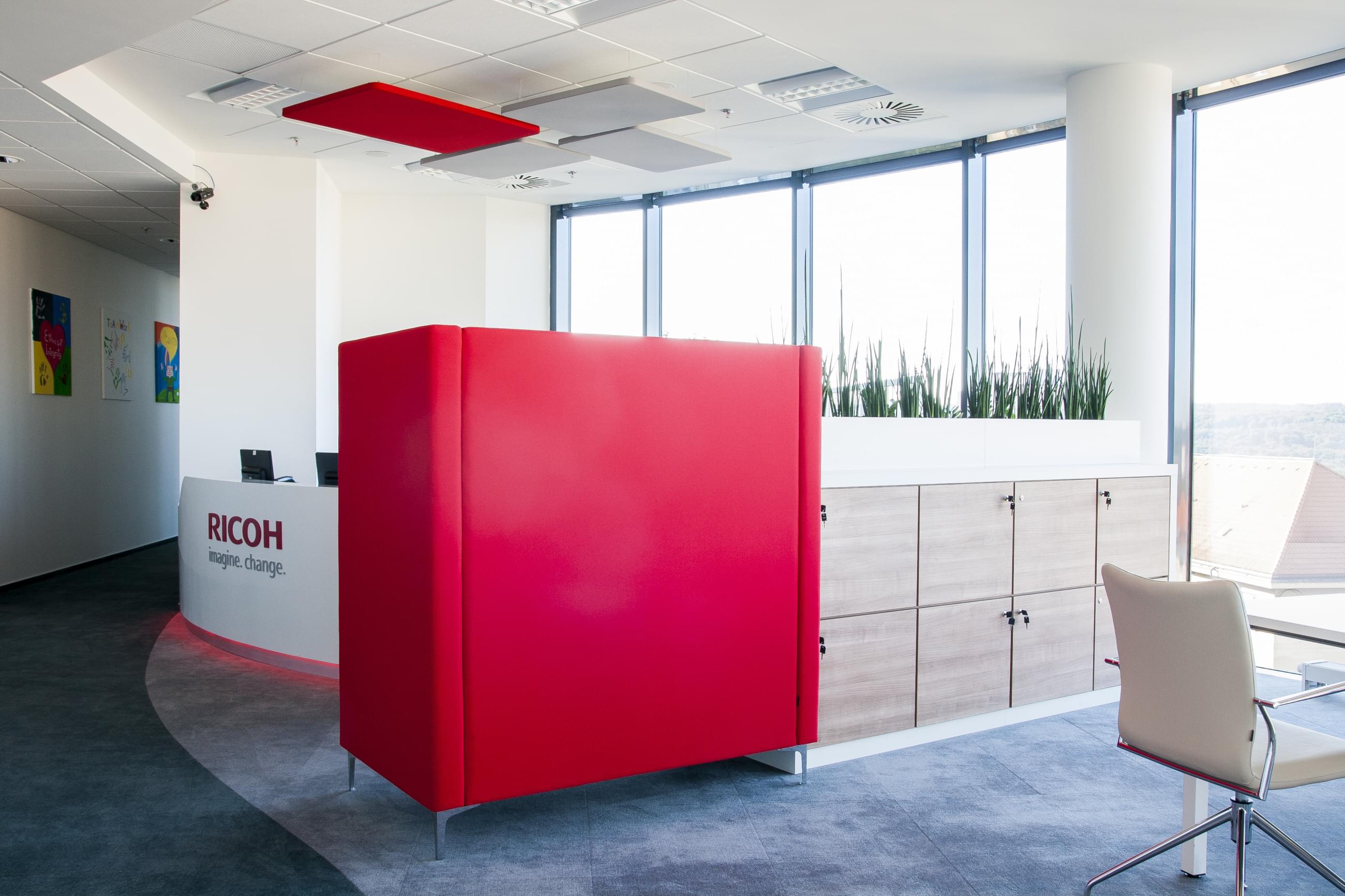  Netradiční interiér kancelářské místnosti firmy RICOH doplňuje pestrobarevná červená úložná skříň. Nechybí ani květináče oddělující pracoviště. 