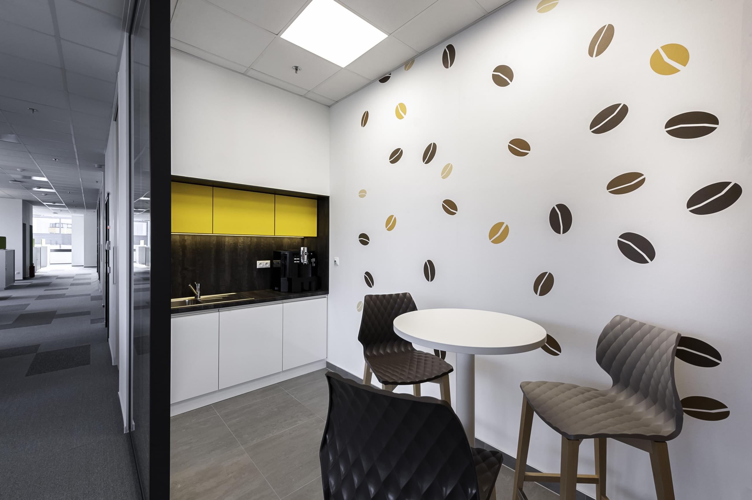 Tapeta podobě kávových zrnek vytváří příjemnou atmosféru a dotváří celkový design v interiéru. Kávová tématika na tapetě zútulňuje kancelářskou kuchyňku. 