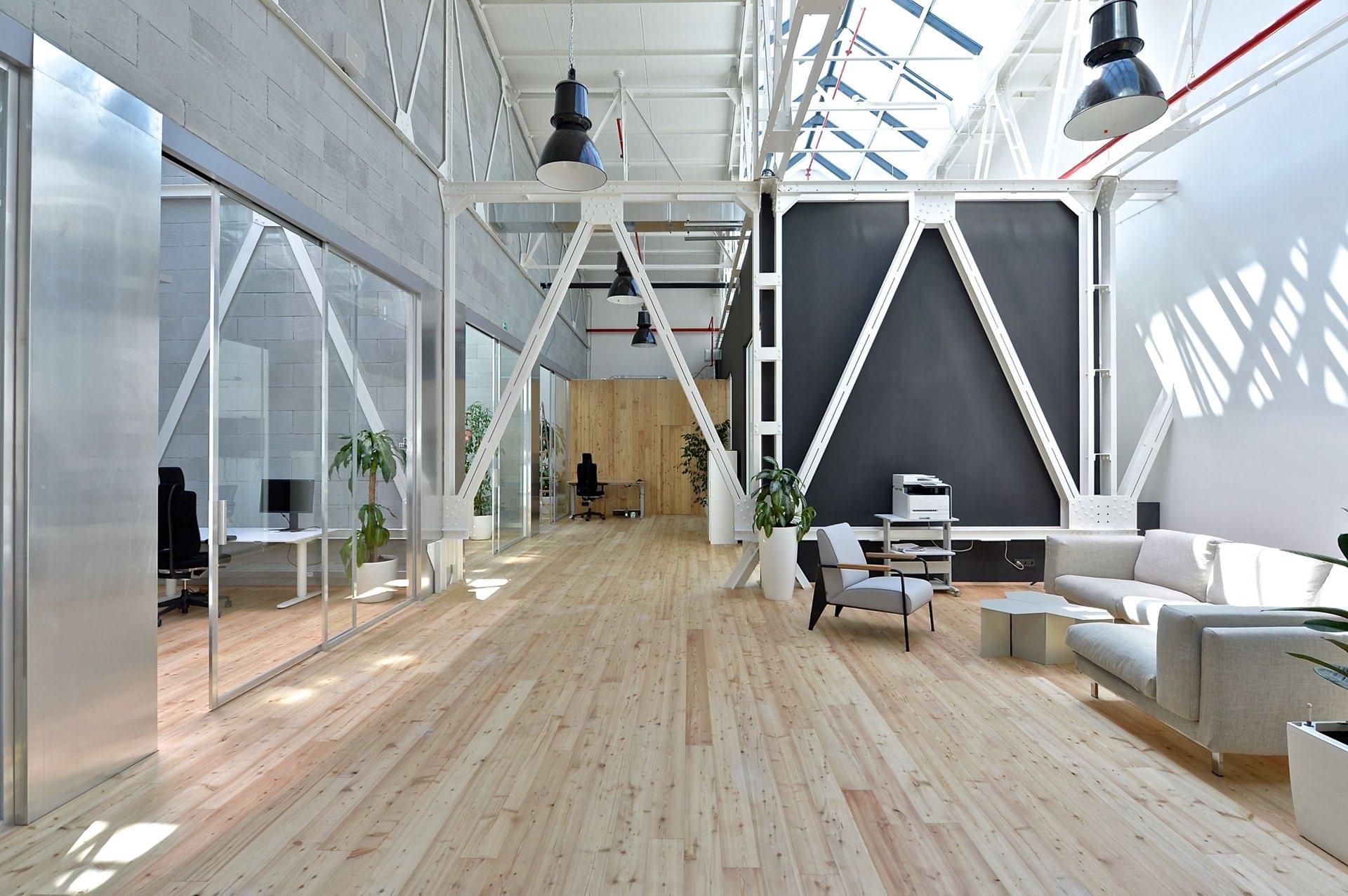 Prostorná místnost s vysokým stropem a moderním interiérem je vhodně doplněná o minimalistické prvky ve světlých barvách, které jsou skvěle sladěny se světlou dřevěnou podlahou. 