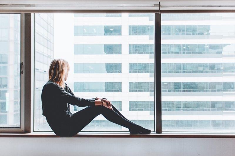 Woman sitting by window with view of office building
