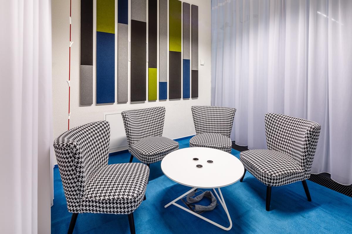 Zasedací místnost tvoří prvky převážně v tmavě modré provedení, přičemž je směle doplňují černobílá kostkovaná křesla.