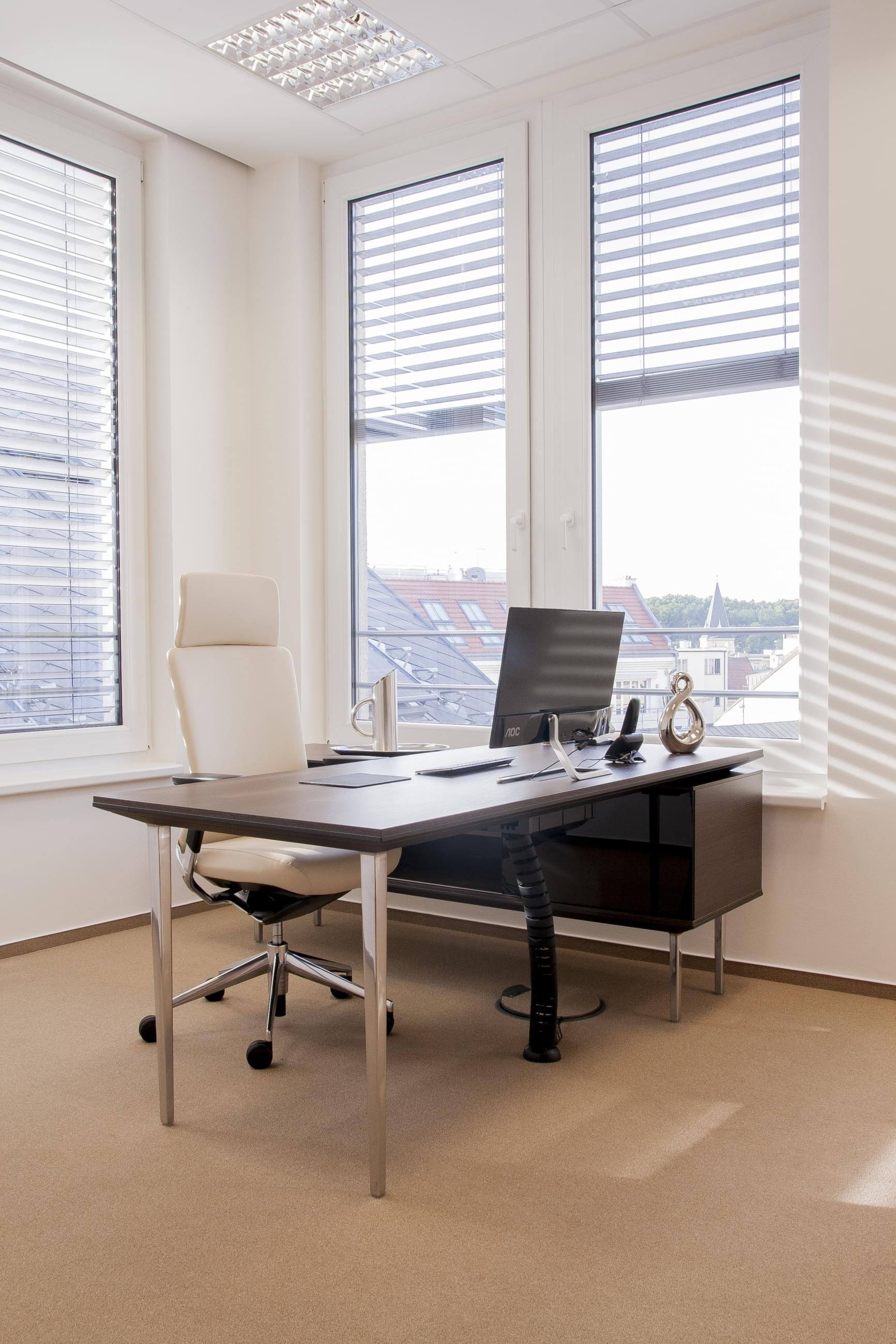 Pohled do manažerské kanceláře provedené v kombinaci chromovaných částí, světle béžového křesla a tmavě dekorovaného pracovního stolu.