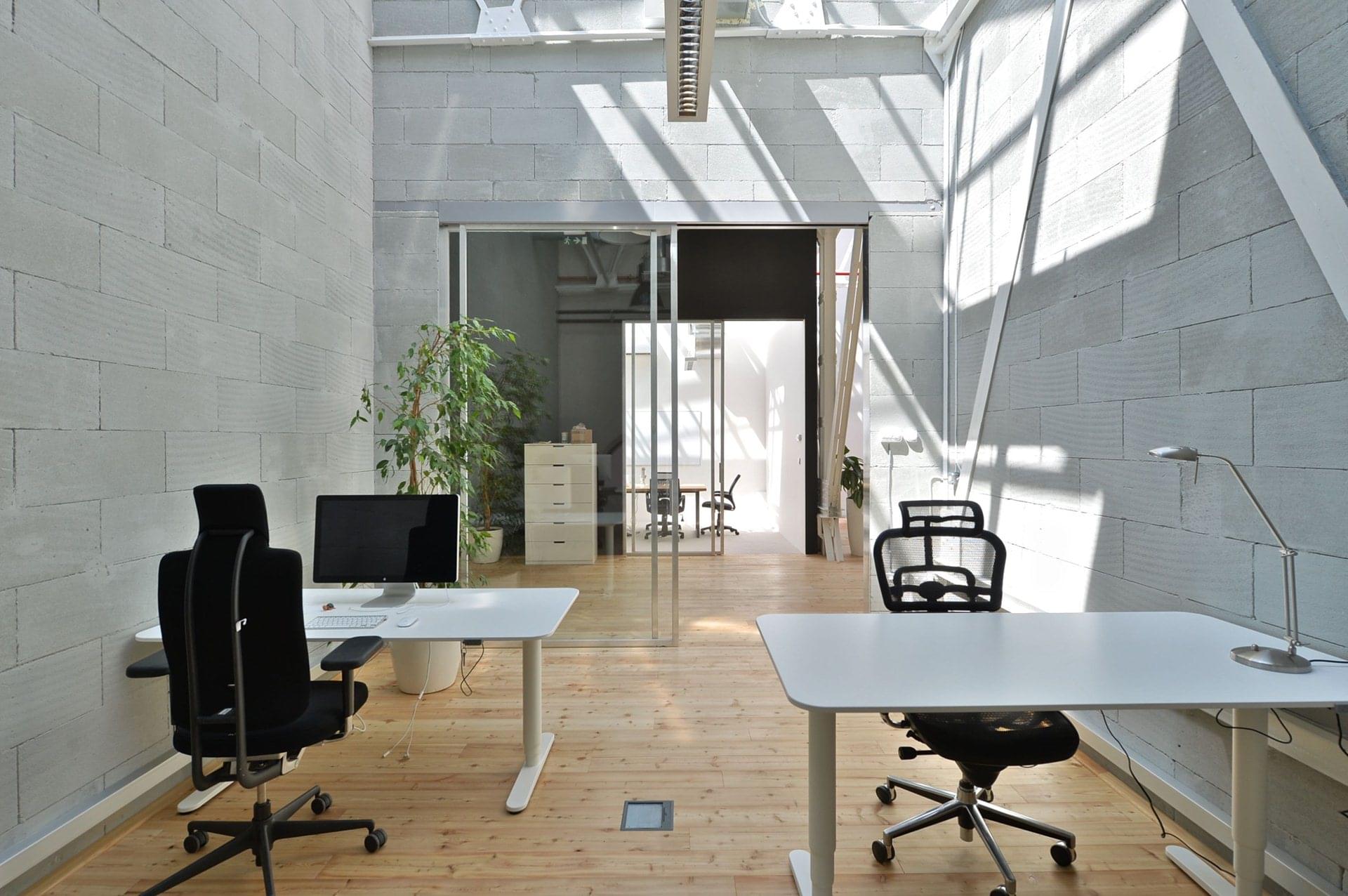 Neobvyklý design kancelářské místnosti s prosklenými dveřmi s jednoduchým interiérem a přirozeným světlem vytvářejícím příjemnou atmosféru na pracovišti.