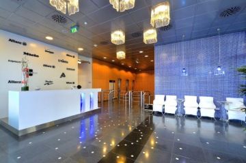 Světlá recepce Diamond Point v pestrých barvách. Na stropě jsou zavěšeny moderní skleněné lampy a u vstupu stojí čtyři bílá křesílka.