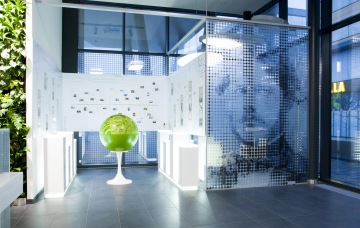 Síň slávy a historie Siemens vytvořená pomocí stěn s fotografiemi a vyobrazením pana Siemense na skleněné stěně.