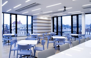 The interior of the cafe at Randstad with white tables and chairs with soft shades of blue, and it all backed by a pleasant view from the glass walls.