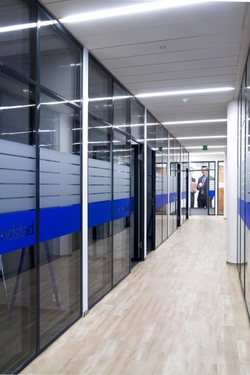 View of the corridor with offices, where the offices are separated by glass walls with stripes of frosted glass for a greater sense of privacy.