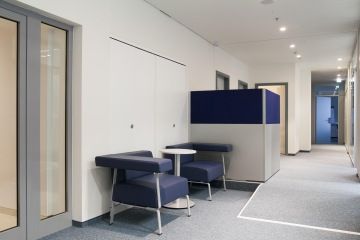 Pohled na rozšířenou část chodby, kam byla umístěna malá odpočinková zóna v podobě dvou designových modrých křesel a praktickým kulatým stolečkem.