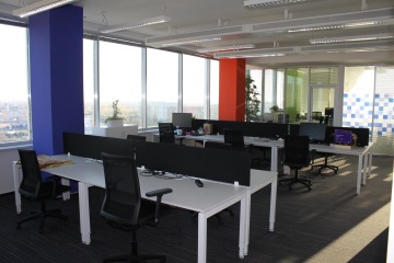 A look at the open space of Concentrix offices with work desks divided by a black divider. Space is dominated by large columns on the wall with windows that are differently colored