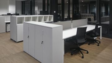 Pracovní místa jsou vybavená bílými stoly, bílými skříněmi a černými židlemi.