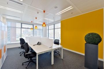 The new offices for Regus in New Park Button Office are equipped with colorful ceiling lights that are fresh thanks to large windows, white tables and yellow painting, in contrast to the green plant in a high gray pot.