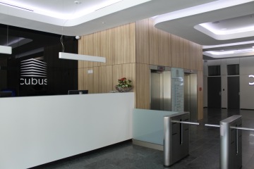 Bílá recepce CUBUS a dominantní černá lesklá stěna s logem. Strop recepce zvýrazňují spuštěné rampy s LED podsvícením.