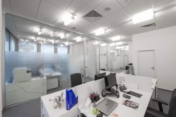 In the Christian Dior office there are white tables and black upholstered office chairs, the space is separated by a glass wall and perfectly illuminated.
