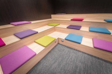 zasedací-místnost-Wargaming-Prague-kaskádovitá-dřevěná-lavice-barevné-podsedáky-CAPEXUS