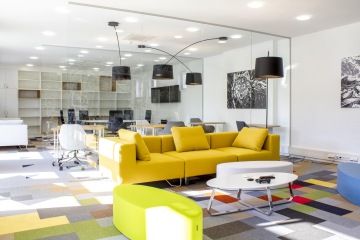 Velmi barevná a prosvětlená relaxační zóna s výraznou hořčičnou sofa, kdy celý tento prostor je oddělen od pracovní části pomocí prosklené stěny.