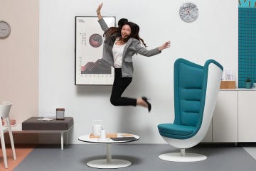 Pozitivně naladěná manažerka ve firmě Actiu zachycena v radostném výskoku se nachází v moderní kanceláři. Kancelář je sladěná do pastelových barev s výrazným tyrkysovo-bílým kancelářským křeslem.