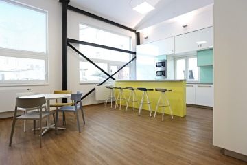 Lesklou bílou kuchyňku doplňuje okrový bar. V jídelní části je nábytkem Actiu v šedé, modré a okrové barvě.