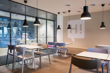 Open space kuchyňka s proskleným výhledem do kanceláří je vhodně laděná do světlých barev. Vše doplňují černá závěsná svítidla.