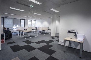 Open space office space is tuned into light colors. Tables with a light wooden board are separated by the beige acoustic panels. On the floor are light gray carpets with dark gray squares.