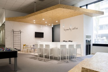 Firemní kuchyňka v bílé barvě s barovým stolem a židlemi s dekorací dřeva