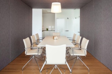 Budova CUBUS má moderní zasedací místnost se světlým nábytkem s kovovou konstrukcí a šedé členité stěny.