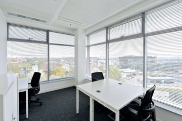 Office Park Nové Butovice has pleasing large offices with lots of light thanks to large windows. The office has a white square table and black office chairs.