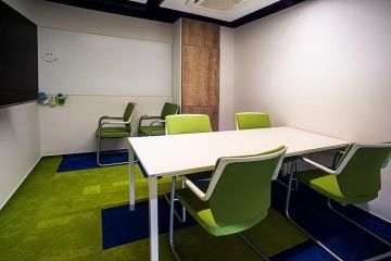A small meeting room for smaller teams with green office chairs, colorful carpet squares and writing boards on two walls.