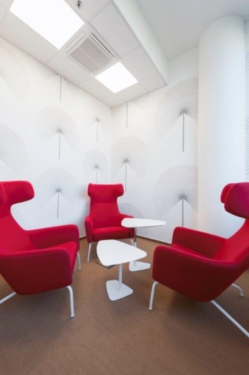 Červený soft seating doplněný o výškově nastavitelné konferenční stolky v bílé barvě s moderně zdobenými zdmi.