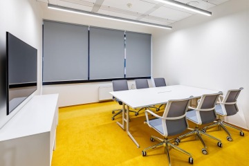 Zasedací místnost v bílo-žlutých barvách a televizí na stěně