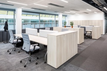 Open space v Sev.En Energy ve světlých barvách oddělený stolními paravány.