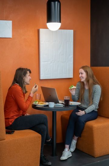 Two women are eating at a round table in a cafe corner