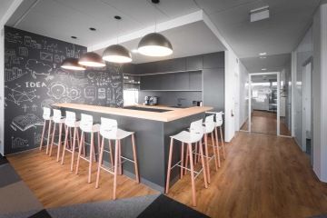 Kavárnu s obsluhou v tmavých tónech rozzáří světlo vycházející ze stropních svítidel ve spojení s dřevěnými a bílými prvky v podobě barového posezení a vinylu.