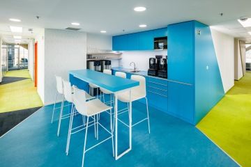Firemní kuchyňka v modrém provedení s barovým pultem a židlemi ve společnosti Siemens
