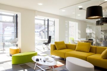 Relaxační zóna s velkou pohovkou v hořčicové barvě a dalšími barevnými prvky interiéru je velmi dobře prosvětlena díky velkým okenním tabulím.