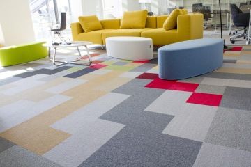 Barevné taburety a pohovka v hořčicové barvě spolu s barevným kobercem čtvercových vzorů podtrhují svěžest relaxační zóny.