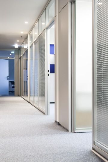 Chodba provedená v kombinaci modré a bílé s částečně prosklenými stěnami oddělujícími jednotlivé prostory.