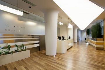 Recepce Clifford Chance s dominantním barisolovým podhledem, kde prostor je kombinací dřevěných parket a bílých ploch s kovovými detaily.