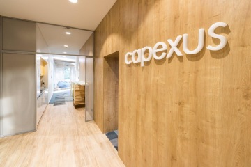 Vstupní prostory nových kanceláří společnosti CAPEXUS v dřevěným obložení a světelným logem.