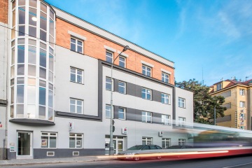 Budova, kde sídlí společnost CAPEXUS, má šedou omítku a výrazný prosklený výklenek.