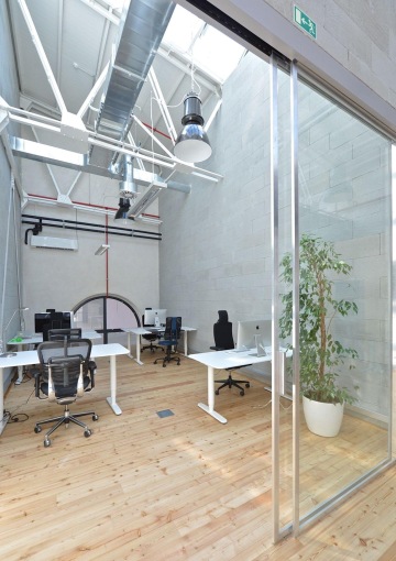 Moderní design kanceláře s nádechem industriálního vzhledu. Vysoké stropy v místnosti vzbuzují pocit vzdušného prostředí. Dekorace ve formě květin dodává místnosti příjemnou atmosféru.