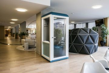 Uzavřený microoffice v podobě prosklené telefonní budky uprostřed kancelářských prostor.