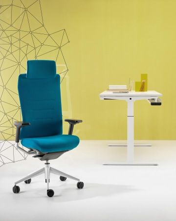 Tyrkysová pracovní židle TNK FLEX splňující ergonomické zásady s polohovatelnou opěrkou hlavy a zad. Vedle kancelářského křesla se nachází výškově polohovatelný bílý stůl.