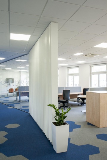 V openspace kancelářích je položen modro-šedý koberec s hexagony, a kaceláře jsou od zbytku prostor nenasílně odděleny skleněnou stěnou a dřevěnými lamelami.